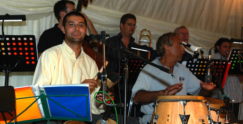 Live Band Jan y su Salsa, bongo player Alejo in the foreground, brass section in the background, at a corporate party in Gloucestershire